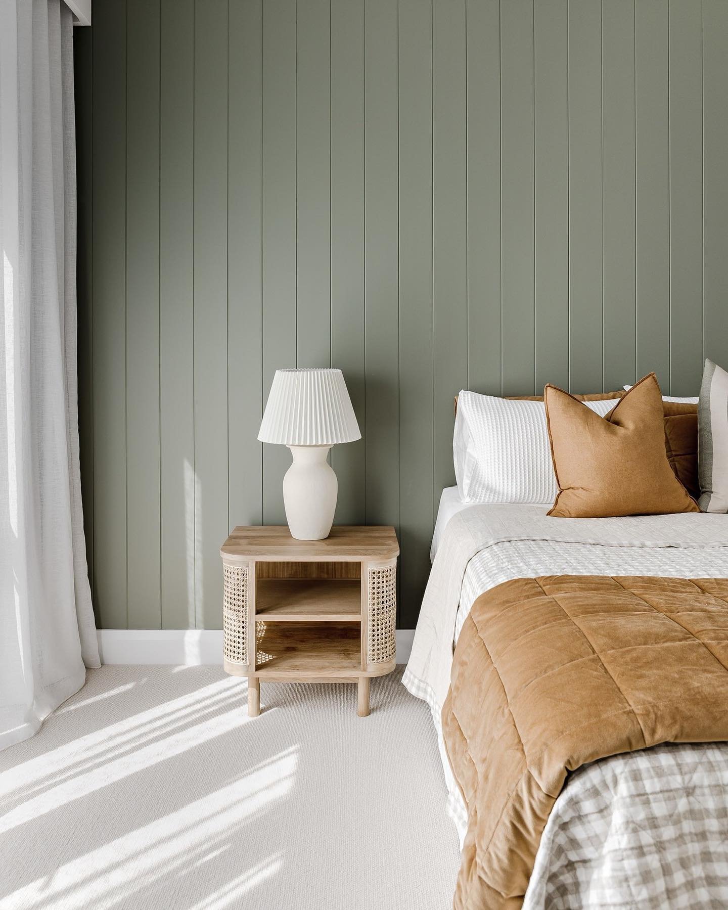 Bedroom featuring vertical tongue-and-groove paneling painted sage green behind a rattan nightstand.
