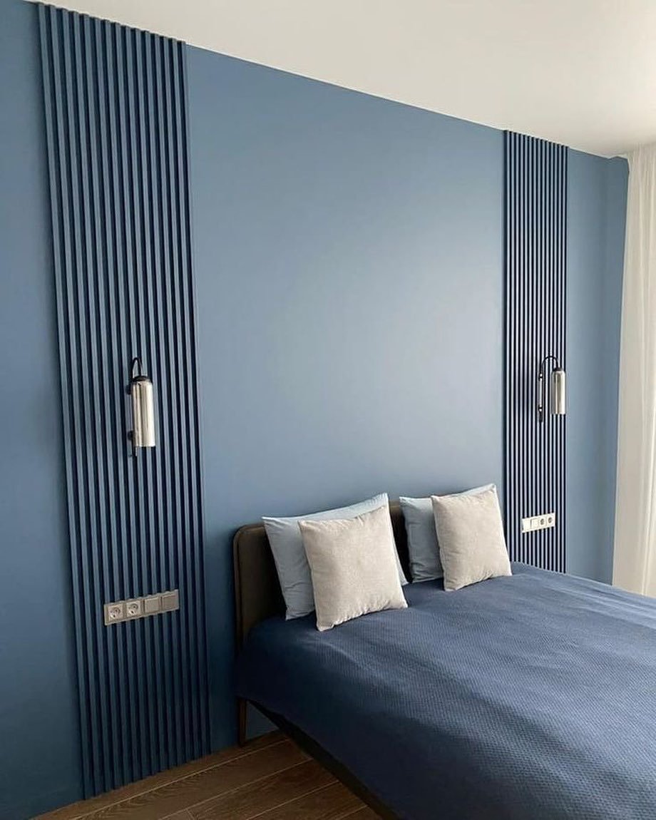 Bedroom featuring a solid blue accent wall with two vertical slatted wood panels and silver sconces.