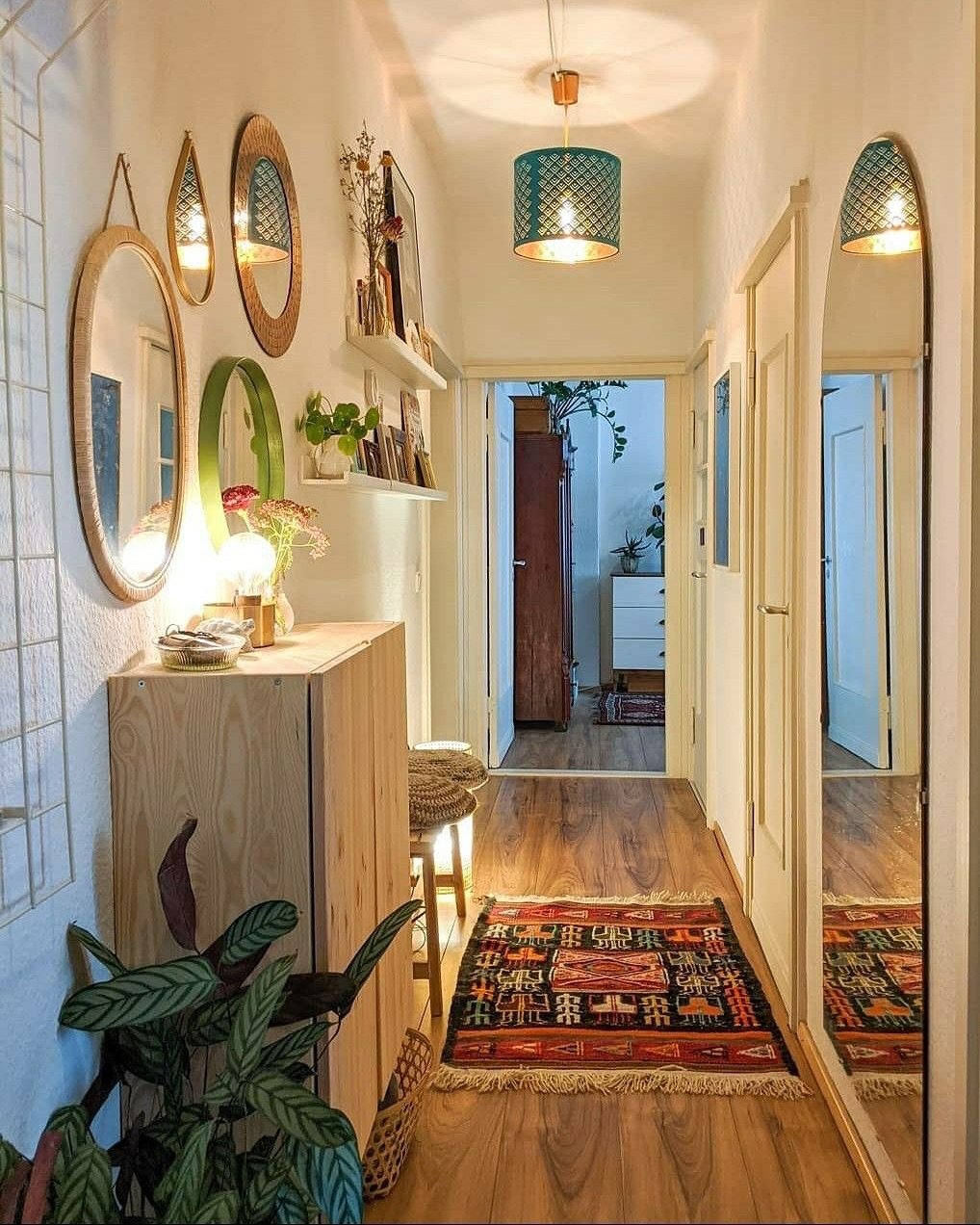A narrow hallway features a gallery wall of mixed mirrors and floating shelves above a wooden cabinet.
