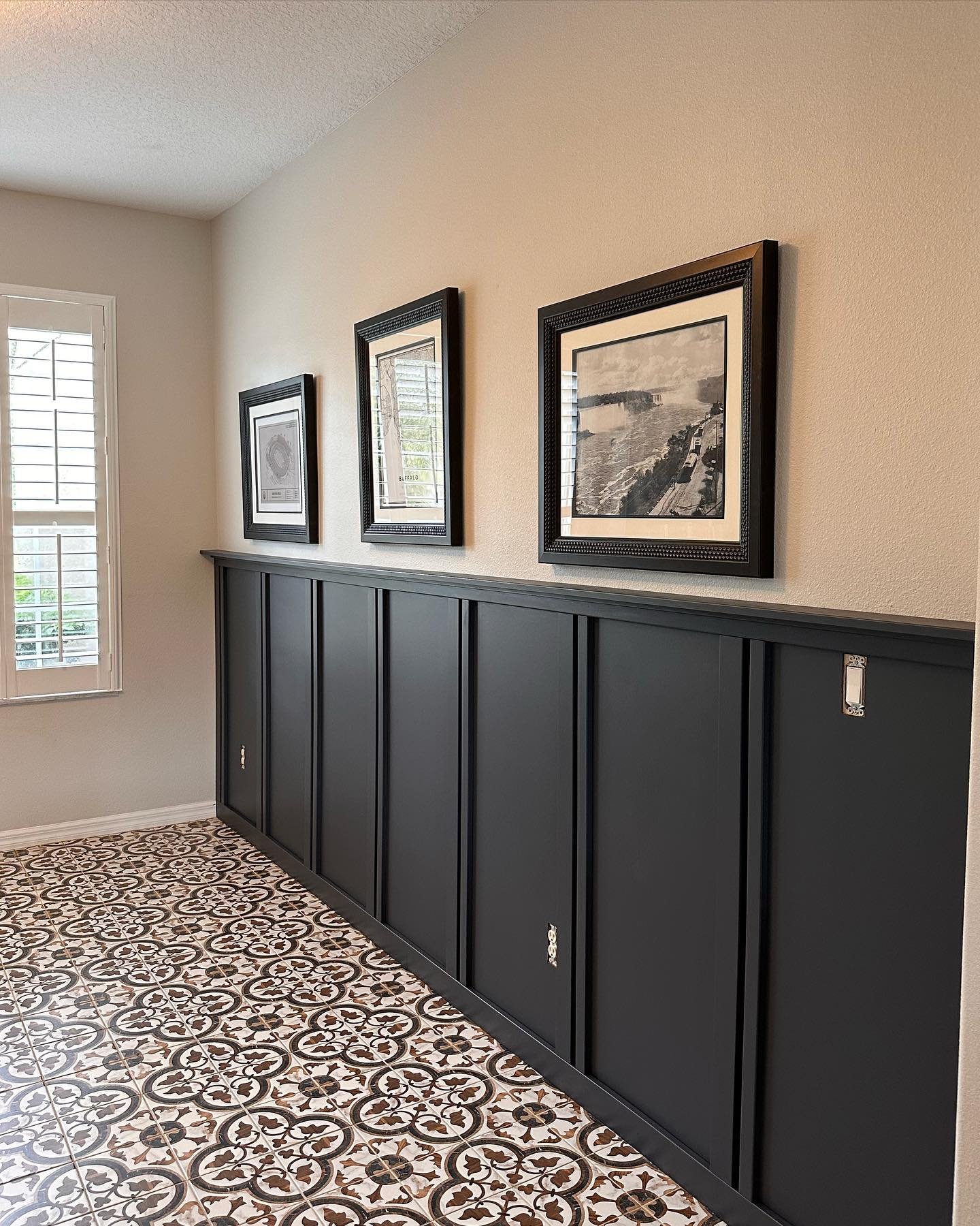 Entryway hallway featuring black wainscoting, patterned floor tiles, and three framed black and white photos.