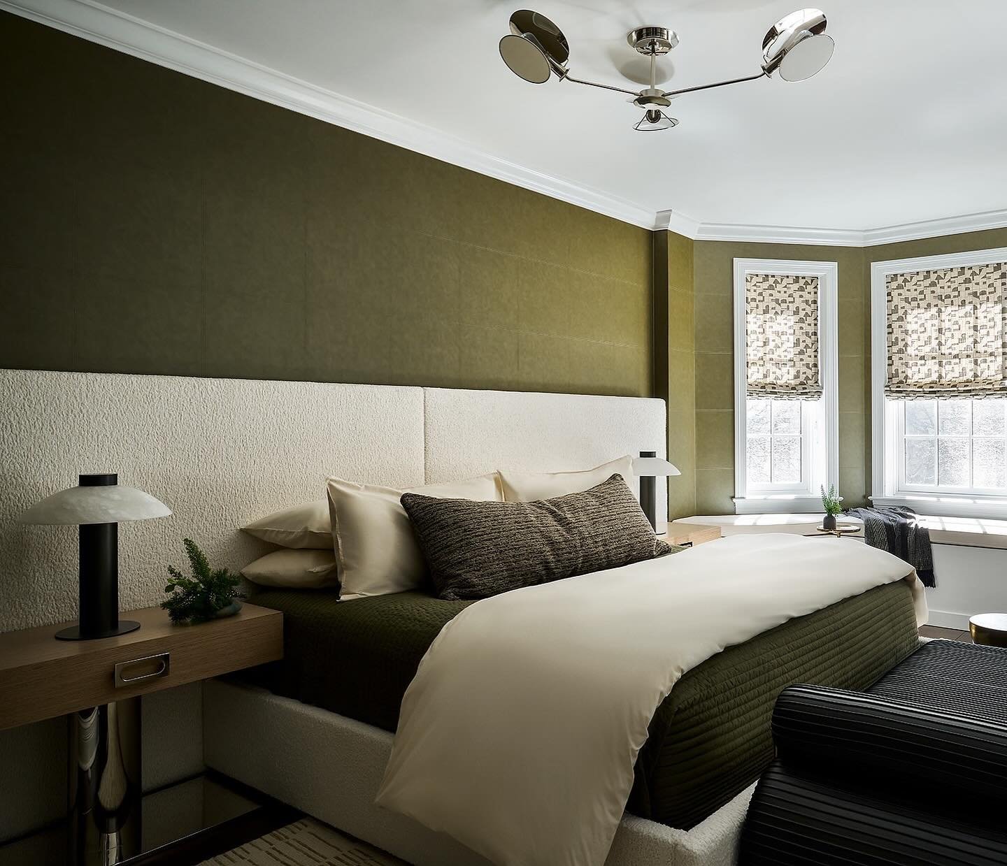 Olive green bedroom accent wall featuring large rectangular panels with a suede-like texture behind a long white headboard.