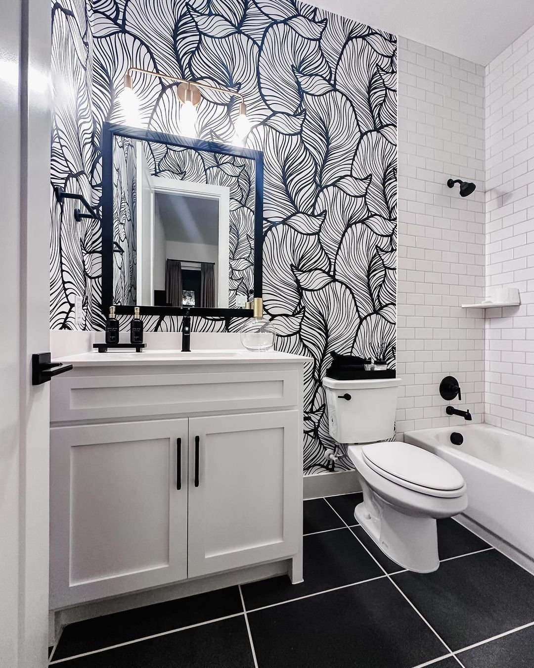 Bathroom vanity area featuring black and white leaf print wallpaper with gold lights.