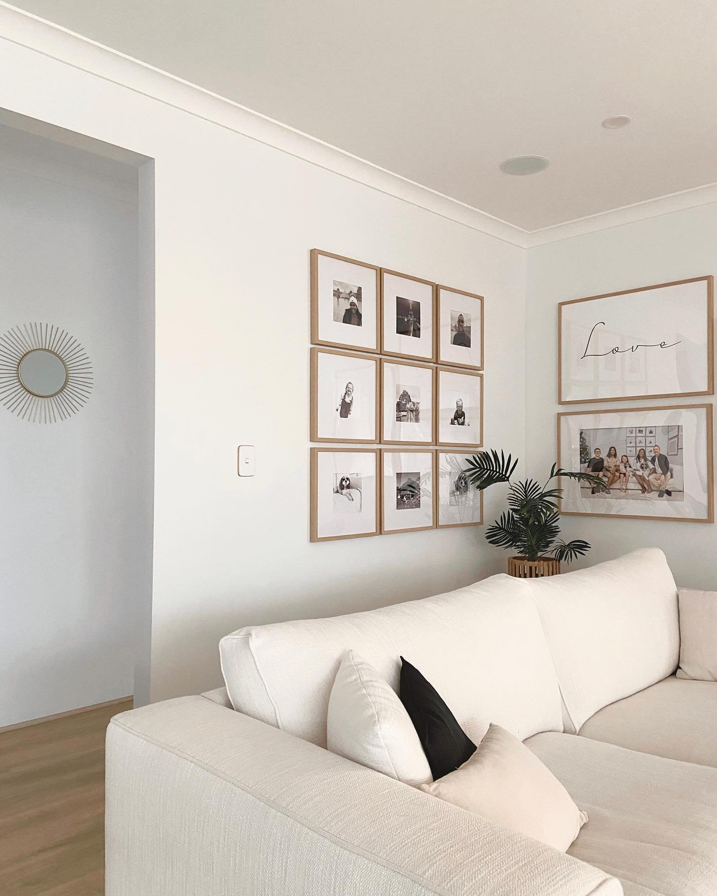 Nine square light wood frames in a grid next to two large stacked frames above a white sofa.
