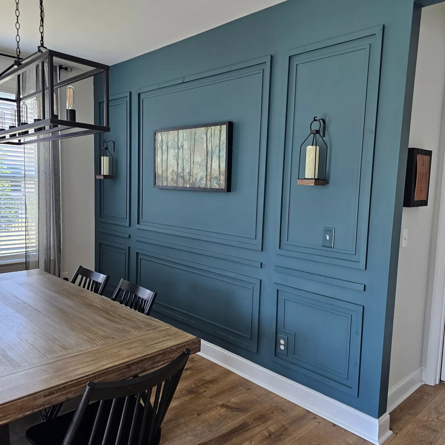 Teal dining room accent wall with picture frame molding and black candle sconces.