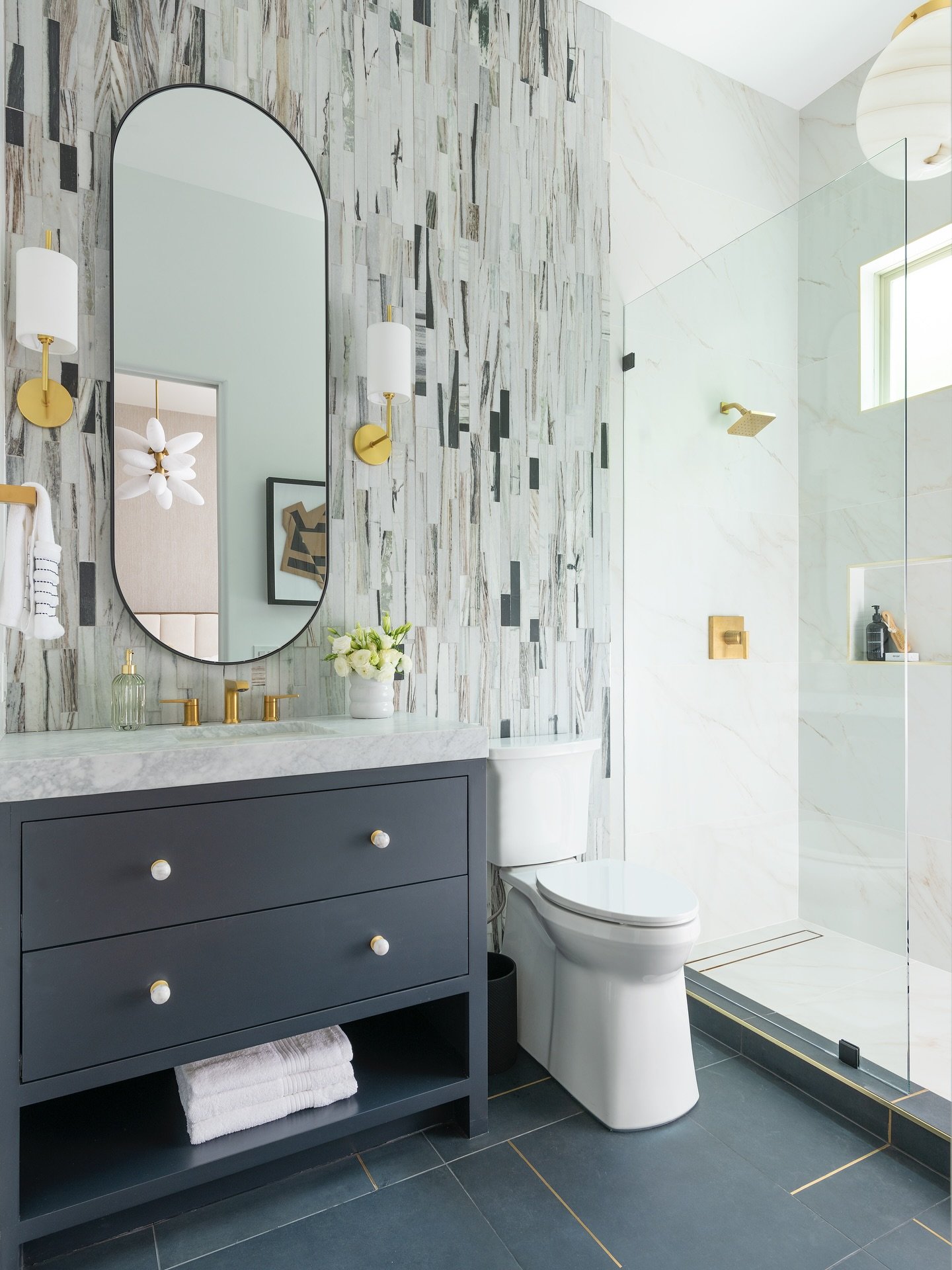 Bathroom vanity with navy cabinet and vertical multi-colored stone tile accent wall.