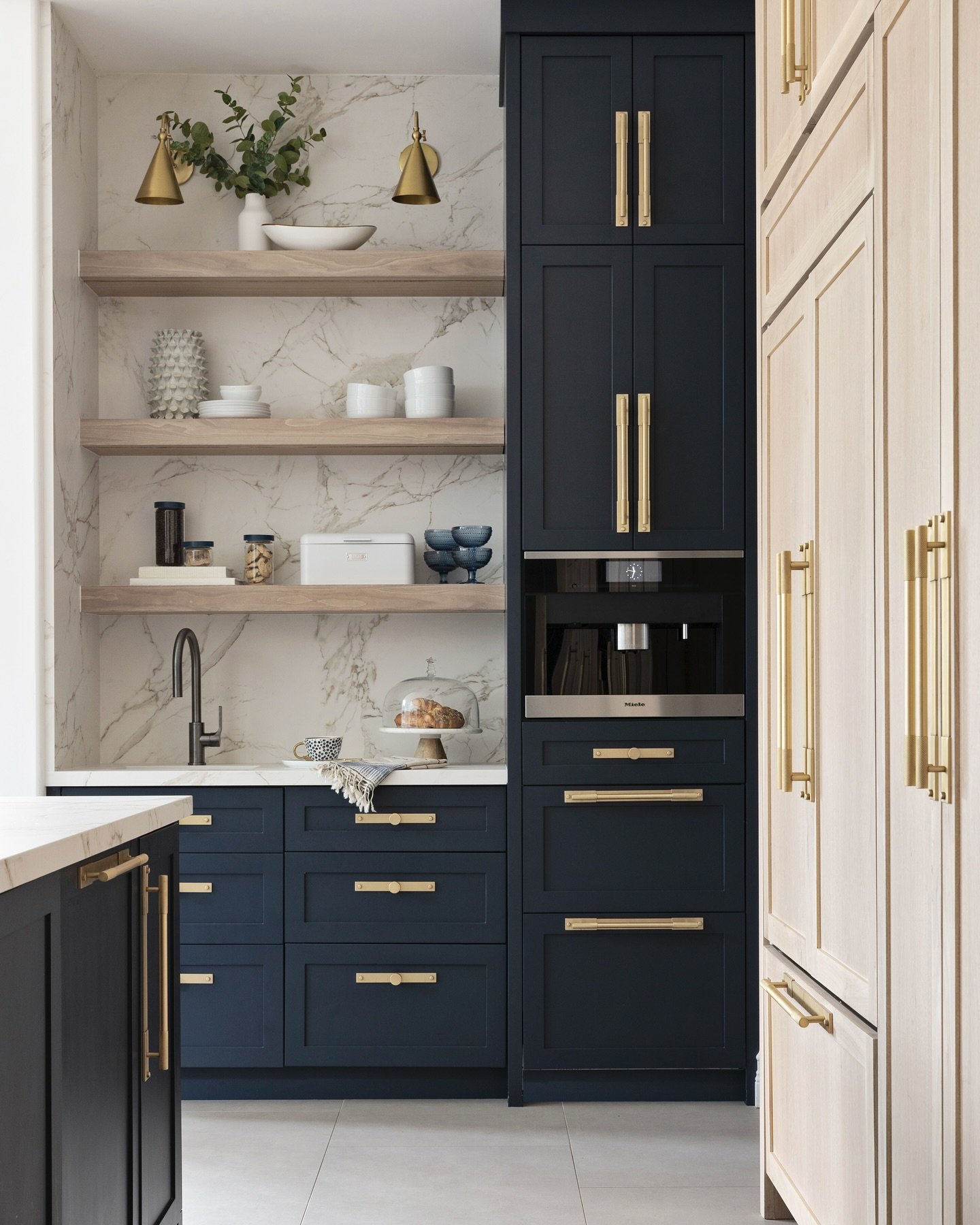 Kitchen wet bar featuring full height marble backsplash and brass wall sconces
