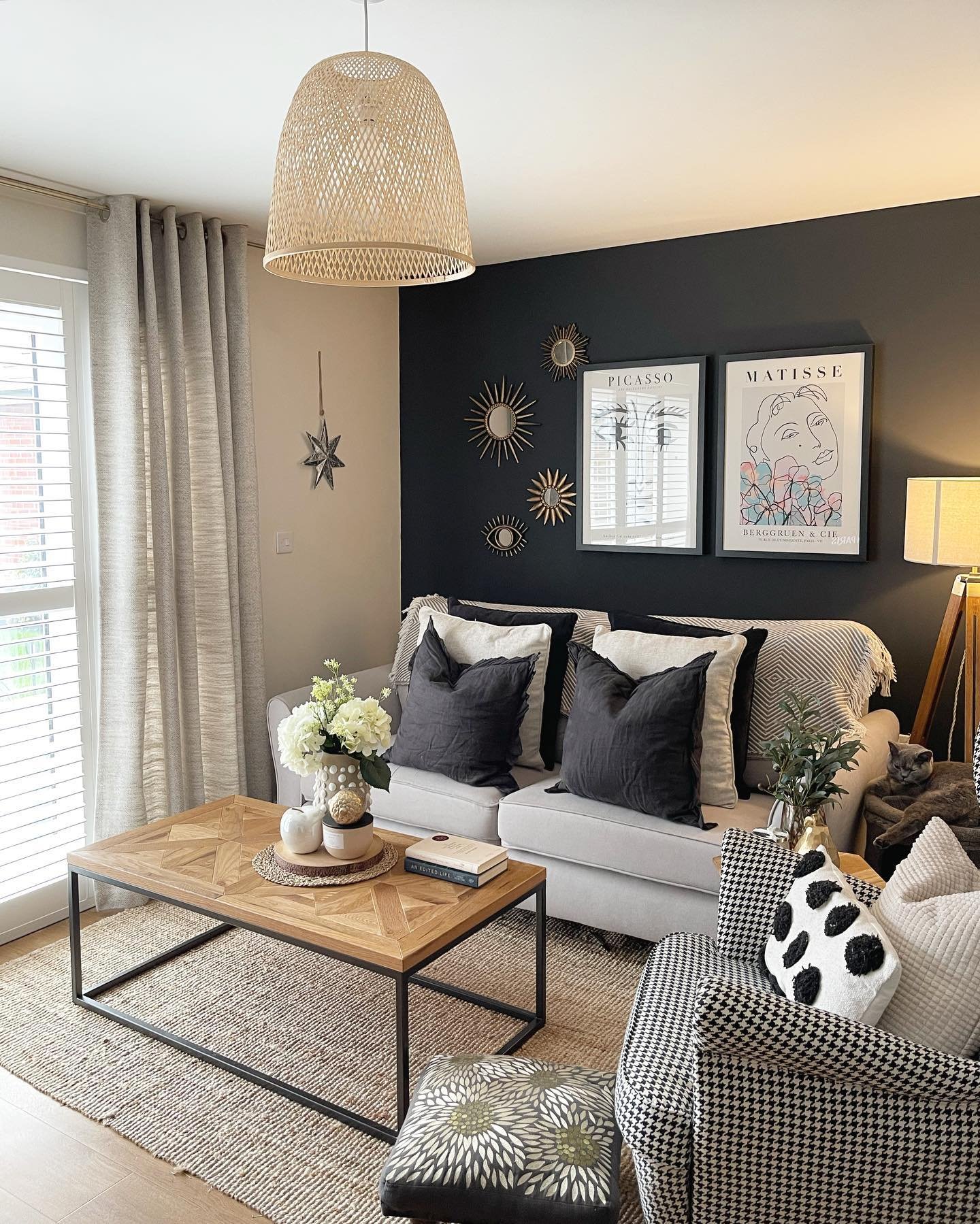 Charcoal accent wall featuring abstract art prints and gold sunburst mirrors above a grey sofa.