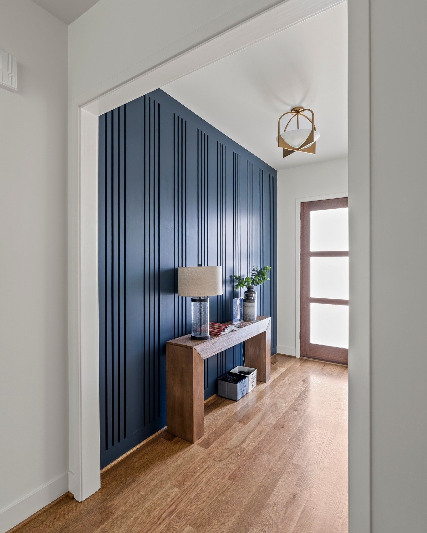 Hallway entryway featuring dark blue vertical slat accent wall, wood console table, and gold geometric ceiling light.