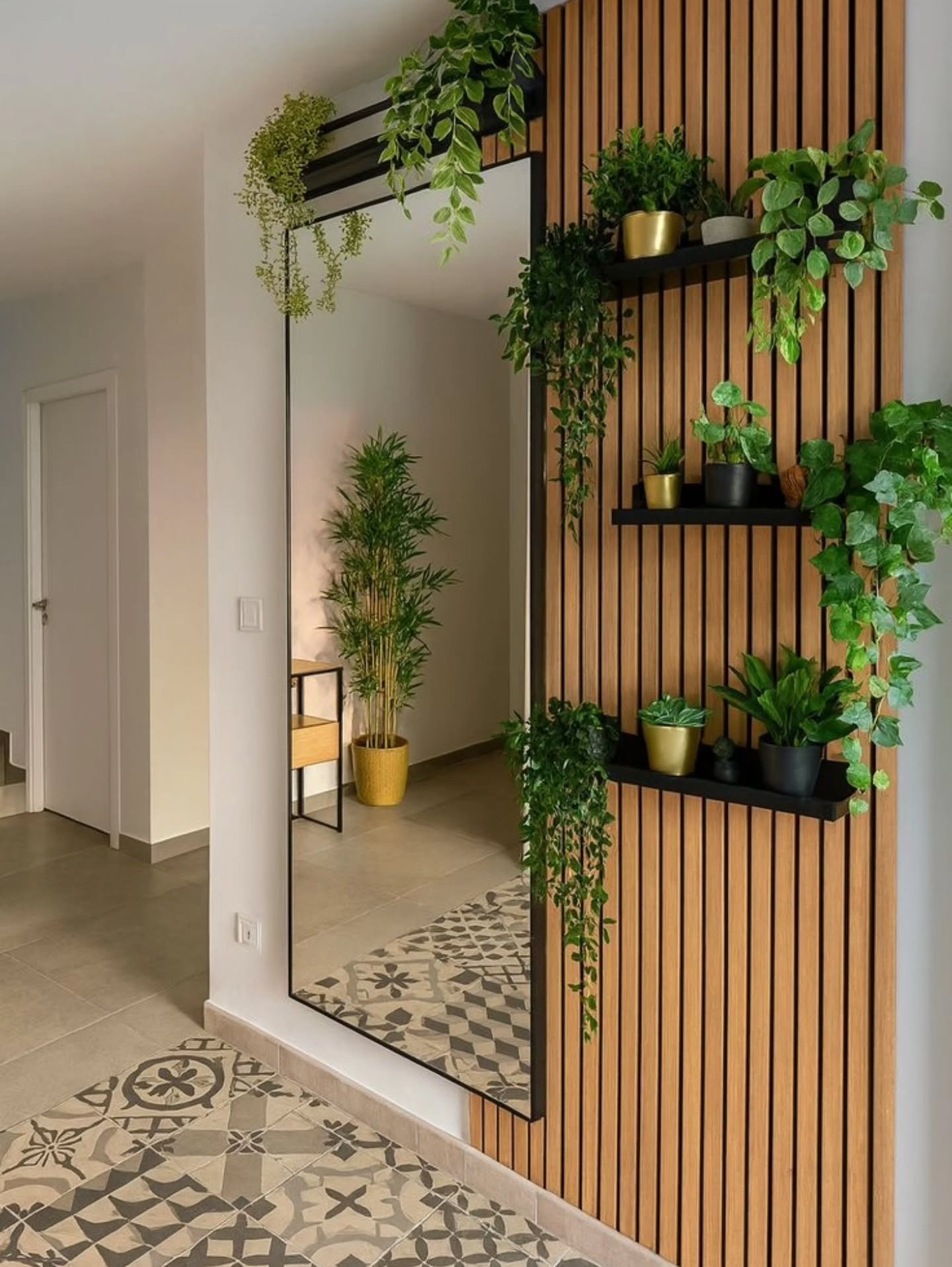 A hallway wall features vertical wood slats with black shelves holding cascading plants next to a tall mirror.
