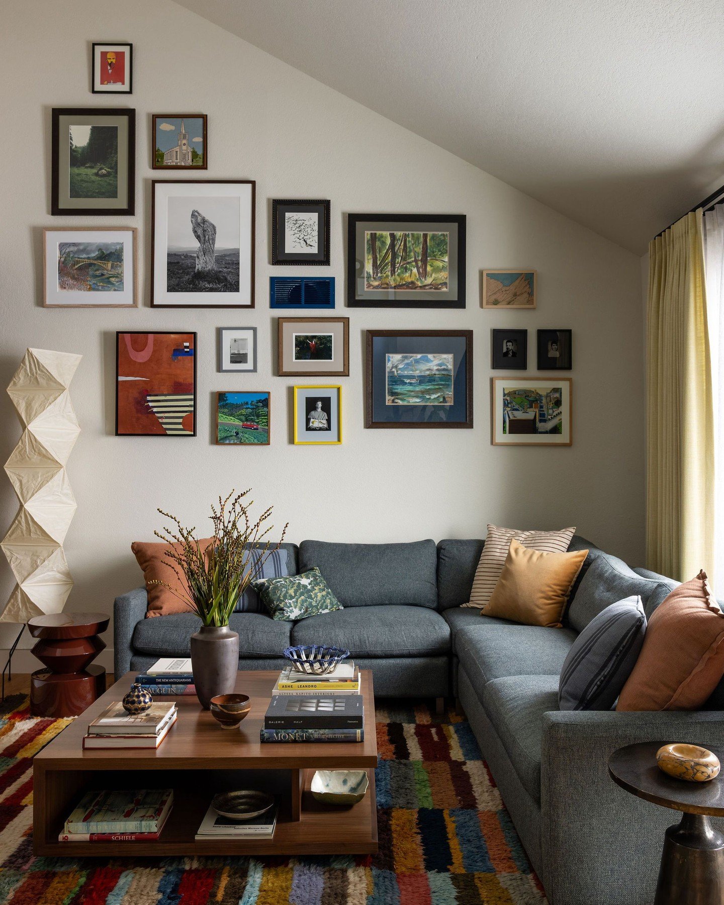 Eclectic gallery wall featuring mixed frames and colorful art following the roofline above a blue sectional.
