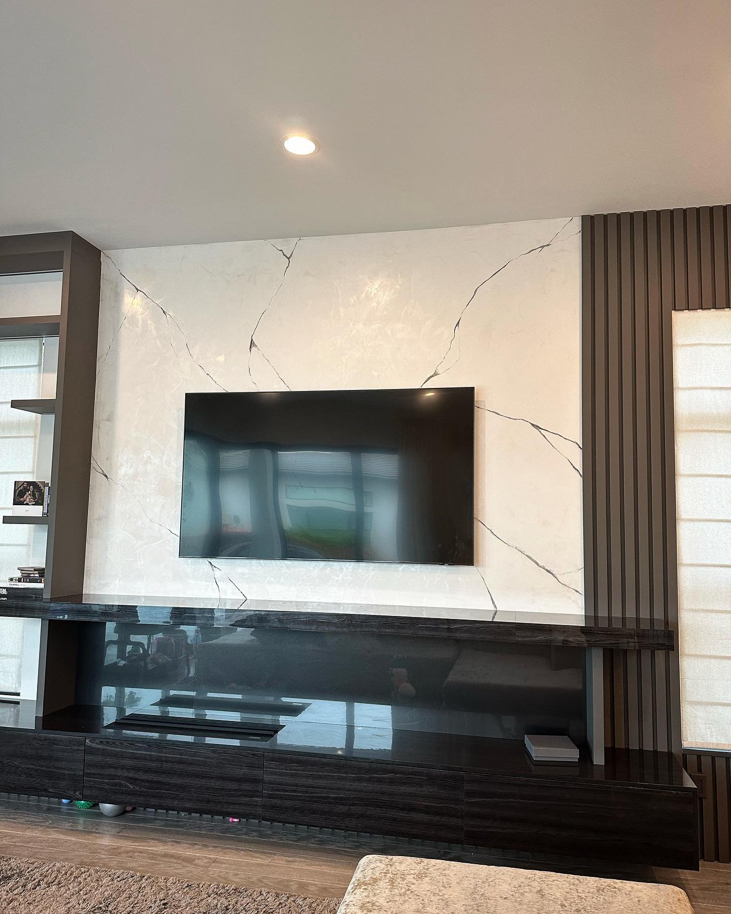 White Venetian plaster TV wall with black veins and dark wood slats.
