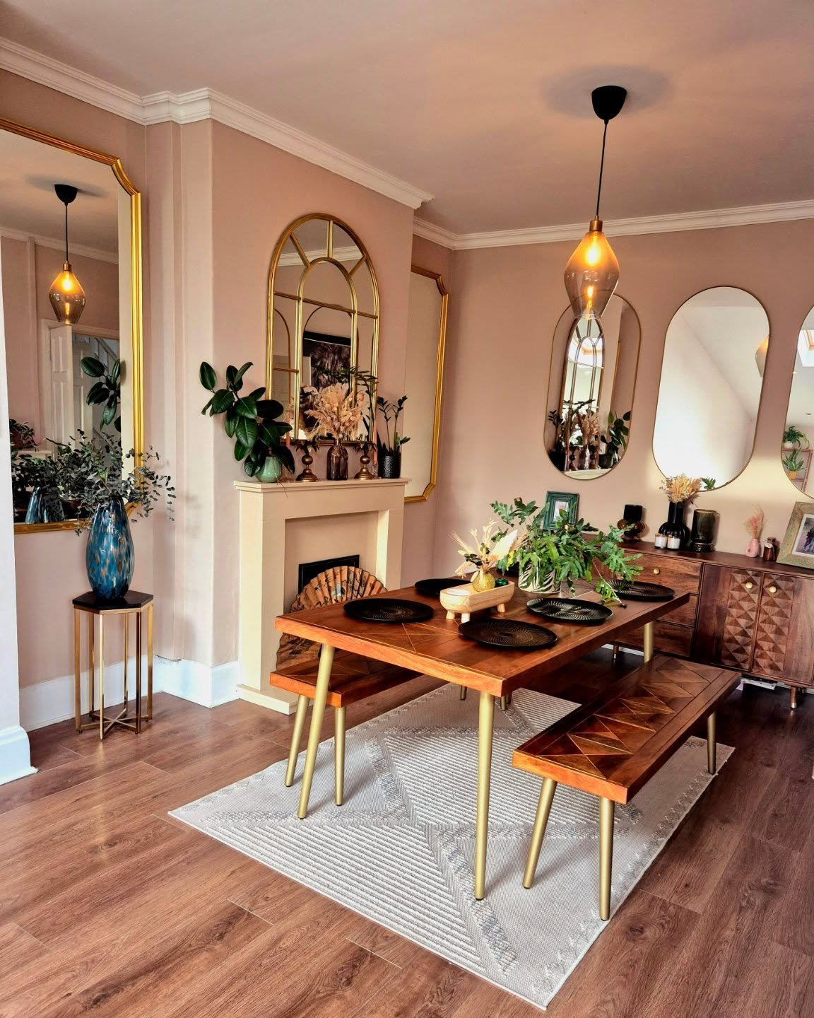 Dining room with pink walls featuring multiple gold arched and oval mirrors over a fireplace