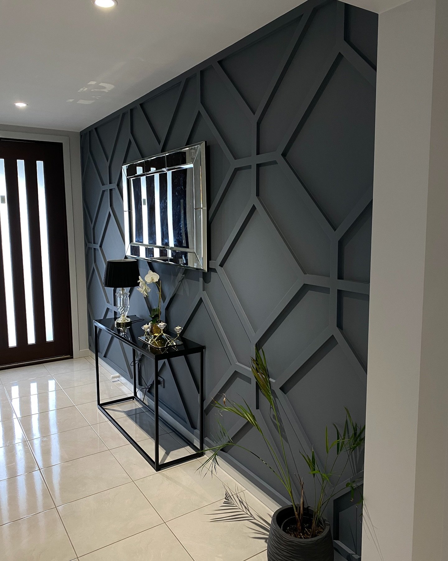 Modern entryway featuring dark grey geometric wall molding, rectangular mirror, and black console table.
