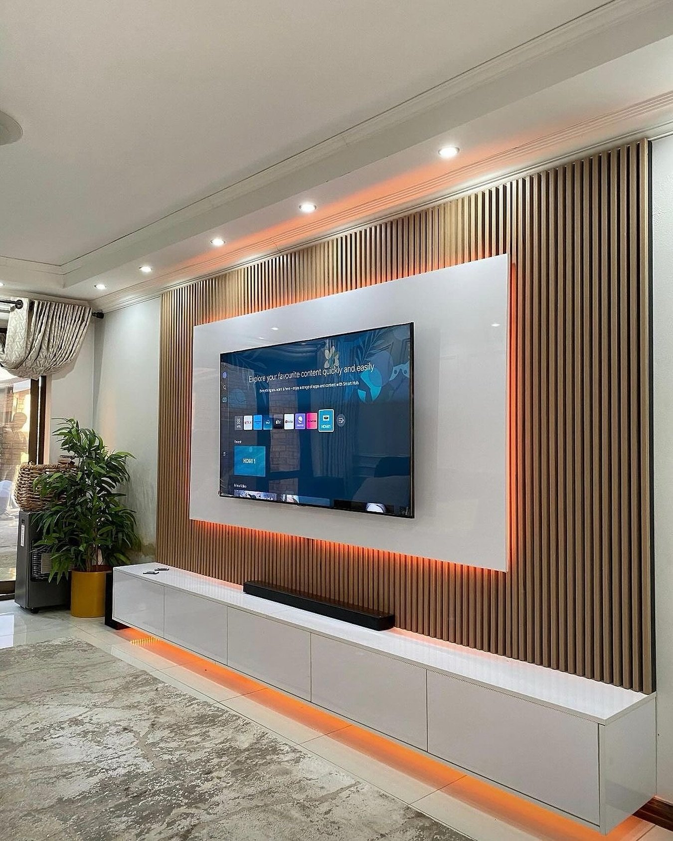 Wood slat TV wall with backlit white panel and floating console.