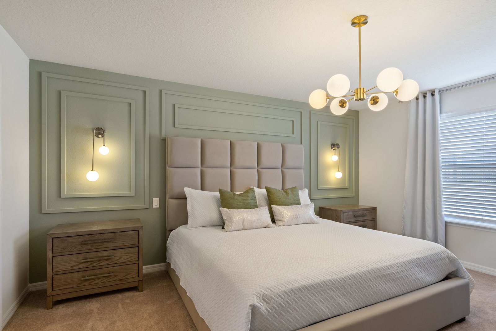 Bedroom with sage green accent wall featuring picture frame molding and brass sconces behind a beige bed.