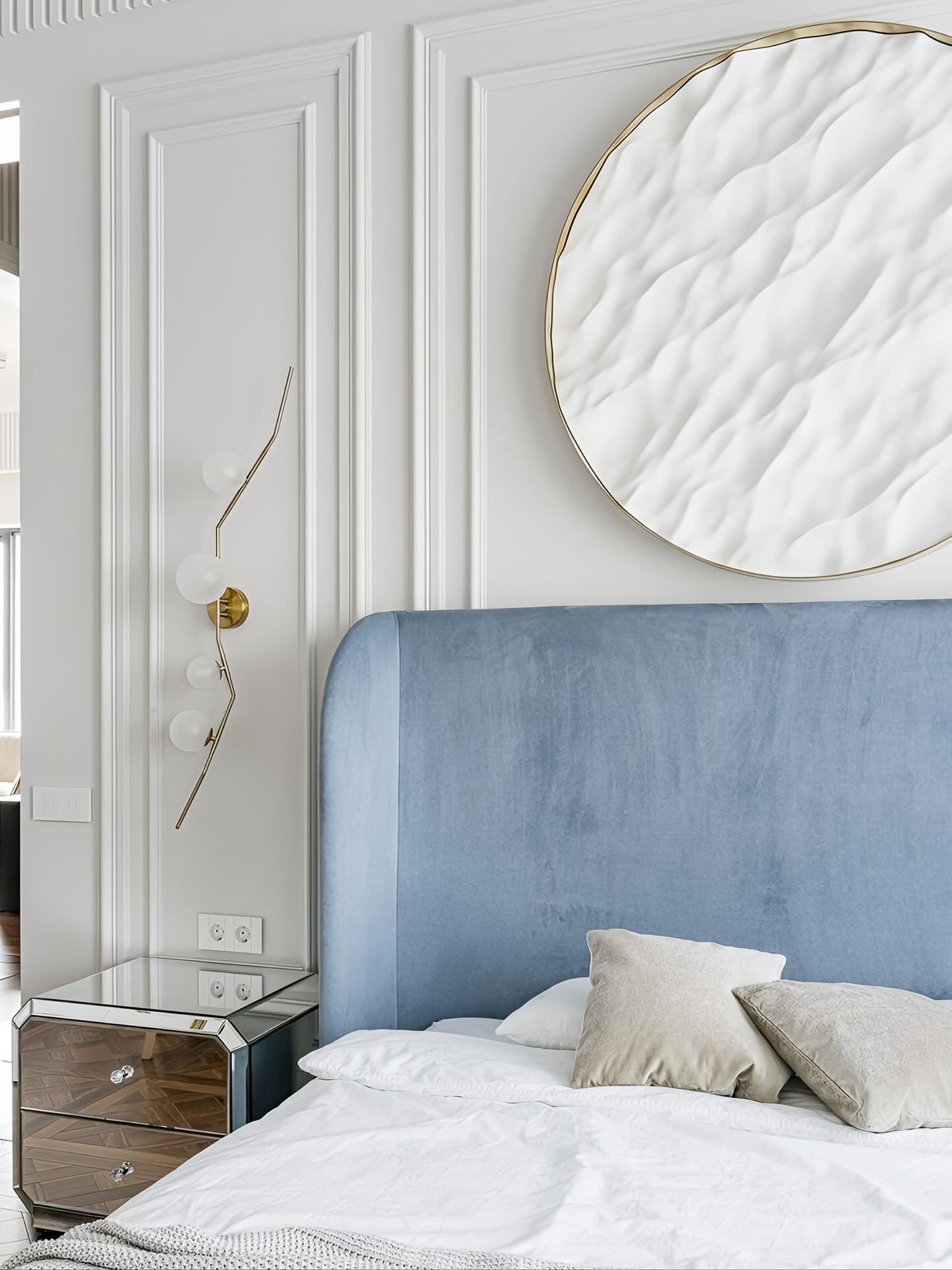 White paneled bedroom wall featuring a large round textured art piece and gold wall sconce