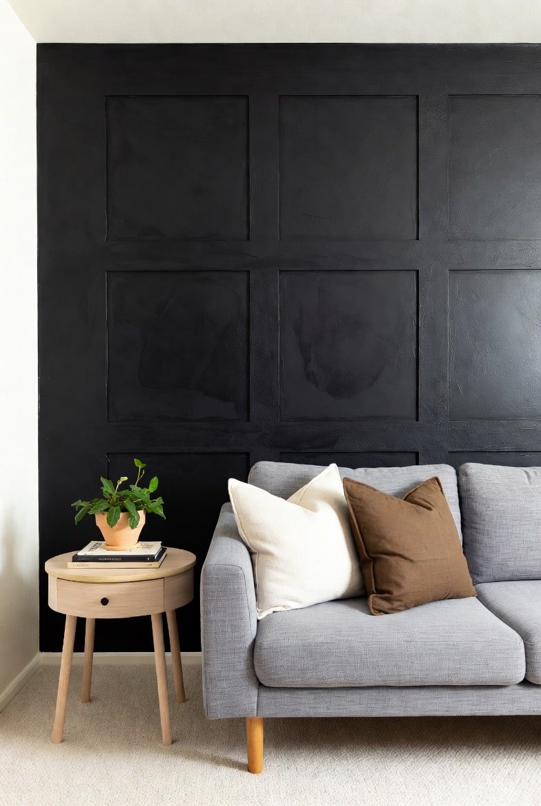 Living room corner featuring a textured black accent wall with square molding, a grey sofa, and a wooden side table.