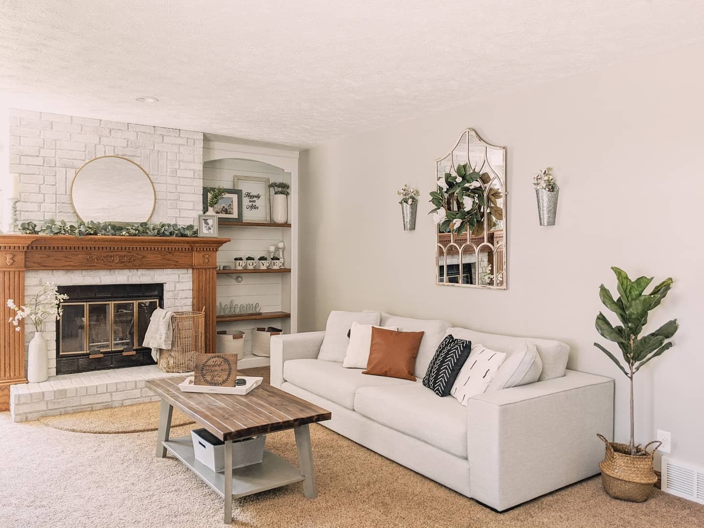 Arched window pane mirror with greenery wreath flanked by metal sconces above a beige sofa.