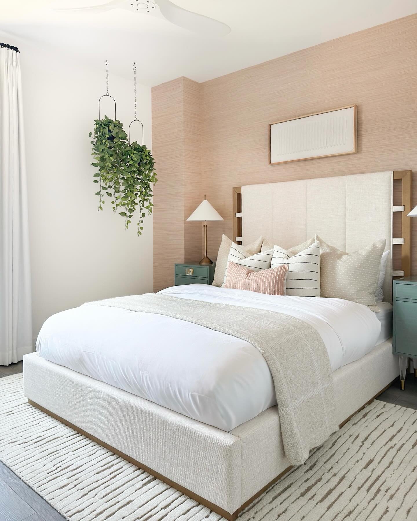 Bedroom featuring a textured soft pink accent wall, white upholstered bed, and hanging green plants.