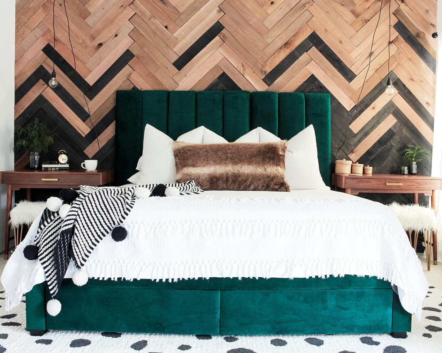 Bedroom with a black and natural wood herringbone accent wall behind a green velvet bed.