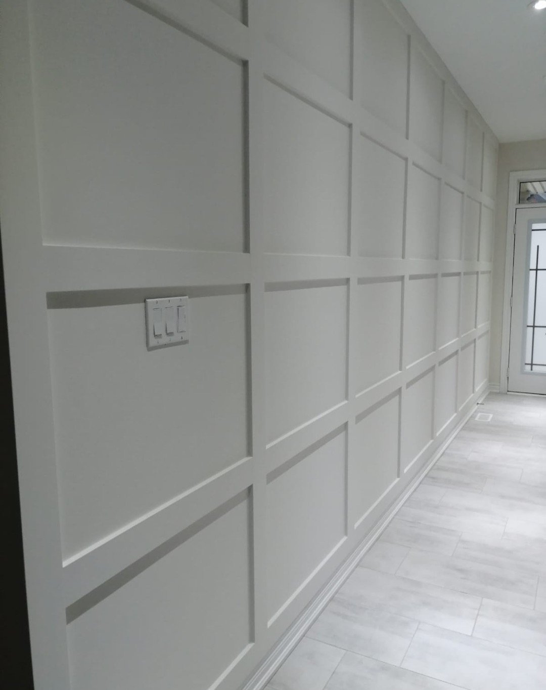 Hallway featuring floor-to-ceiling white square grid wall molding and light tile flooring.
