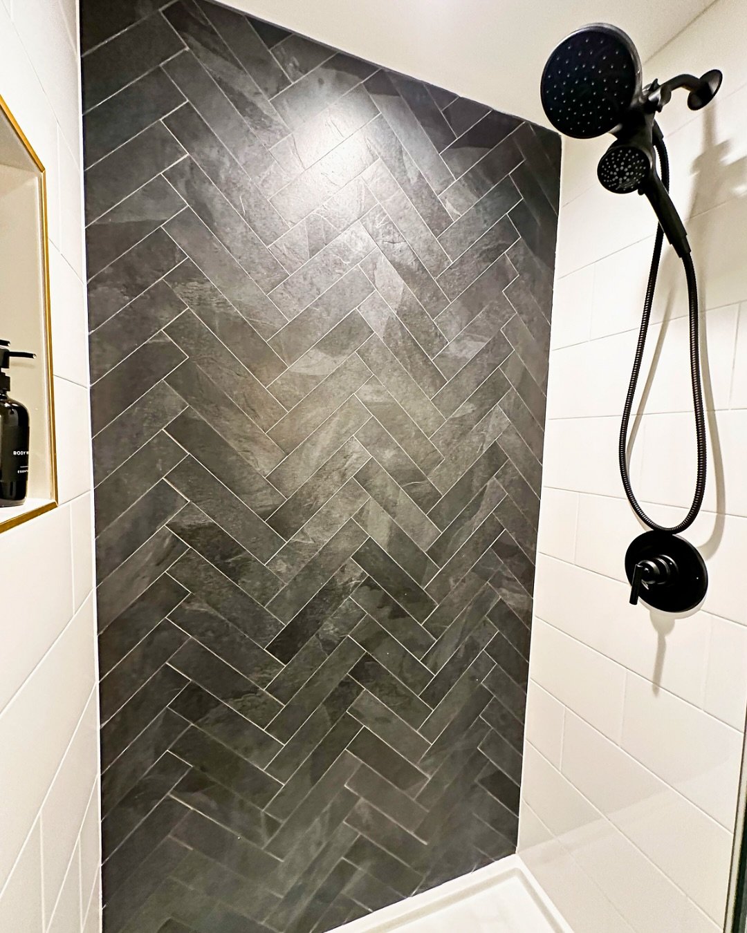 Shower with dark grey herringbone tile accent wall and black fixtures.