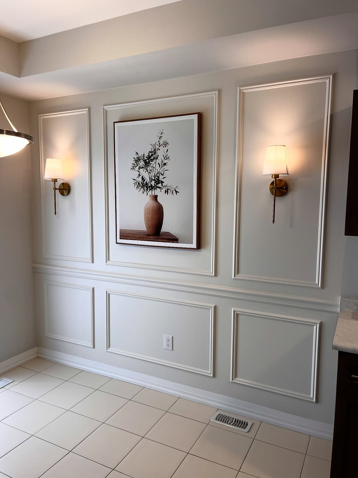 Beige dining room accent wall featuring picture frame molding and brass sconces.