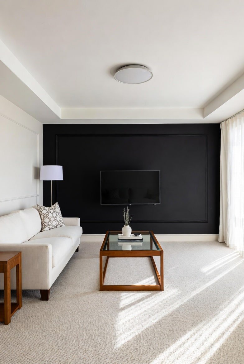 Living room featuring a paneled Black Accent Wall with large box molding, a white sofa, and a glass coffee table.