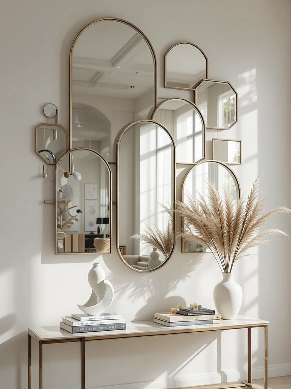 Wall collage of gold-framed arched and geometric mirrors arranged above a white console table with pampas grass décor.