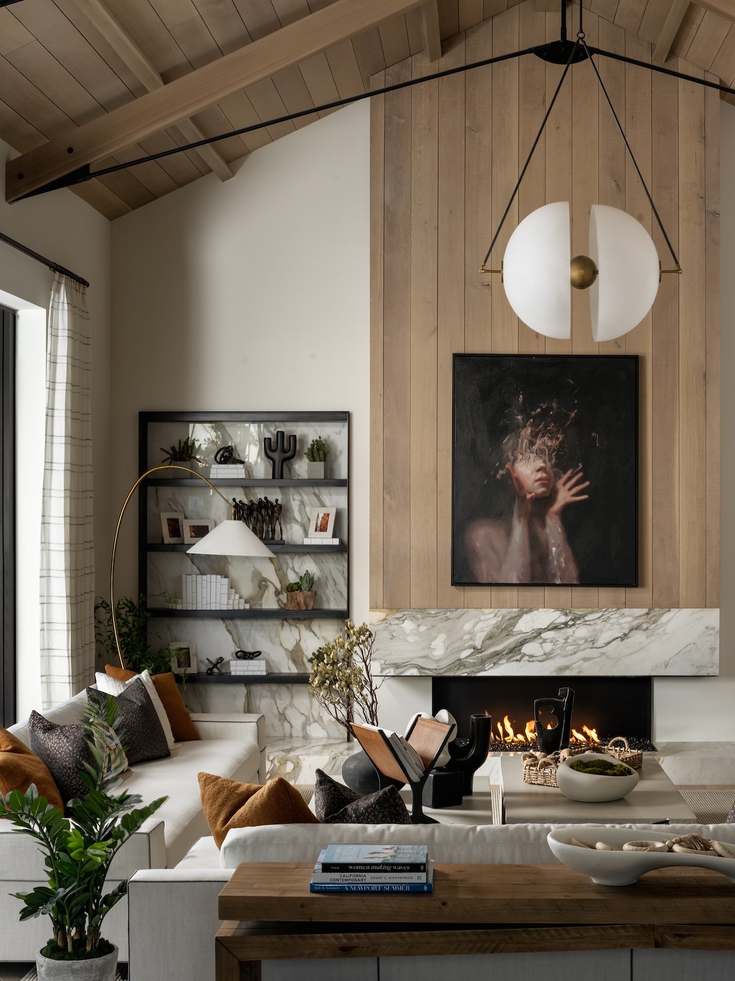 Modern white split-globe pendant light hanging in a living room with vaulted wood ceilings.