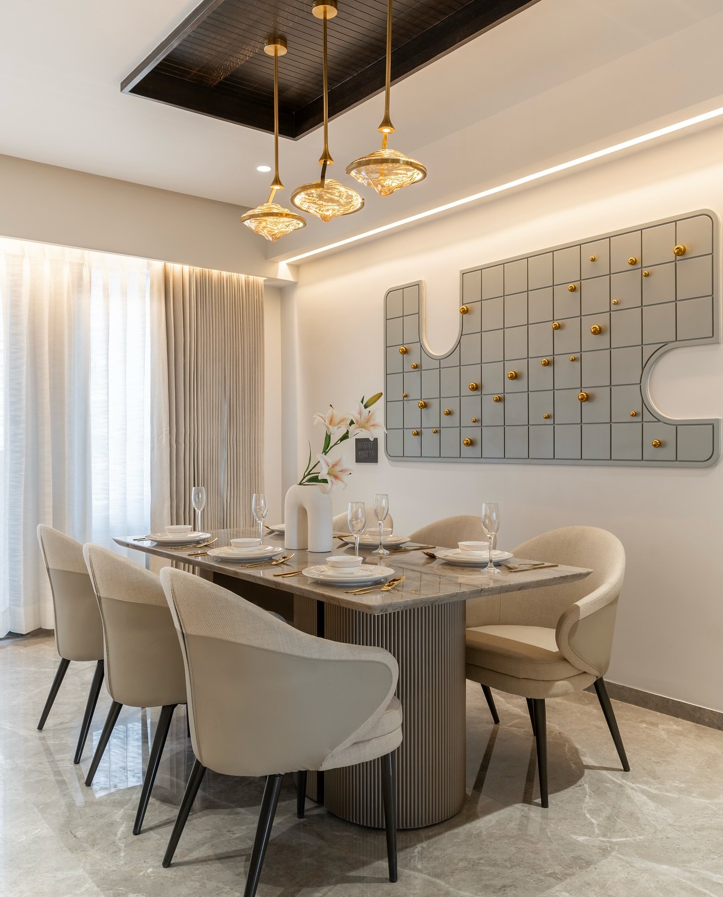 Gold pendant lights hanging over marble dining table with grey wall decor.