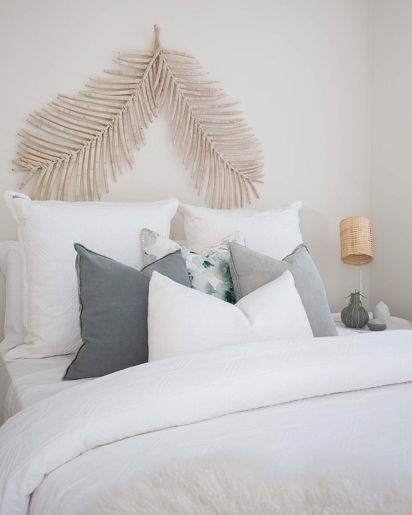 Whitewashed dried palm leaf wall art above white bedding
