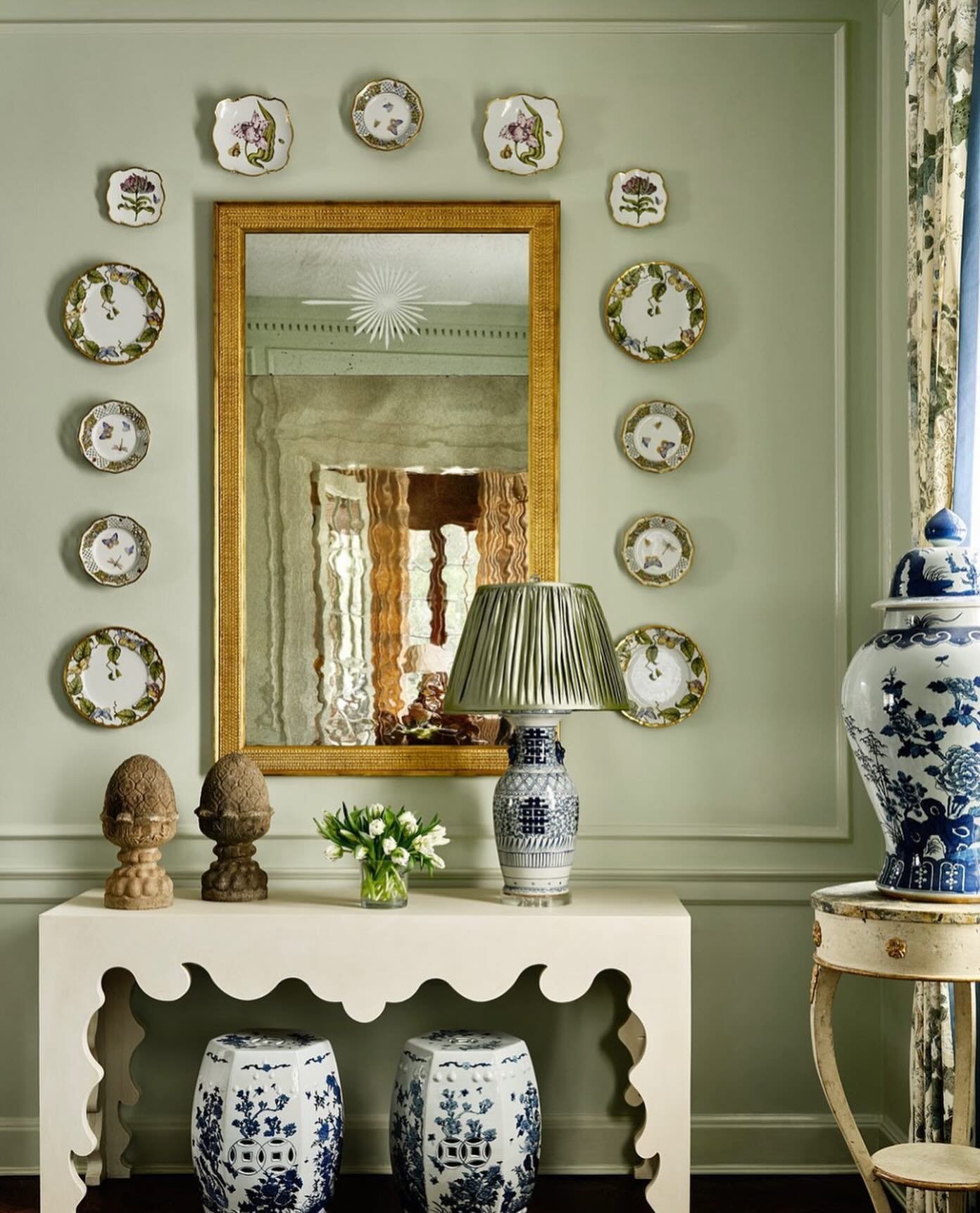 Pale green wall featuring a rectangular gold mirror surrounded by small floral botanical plates