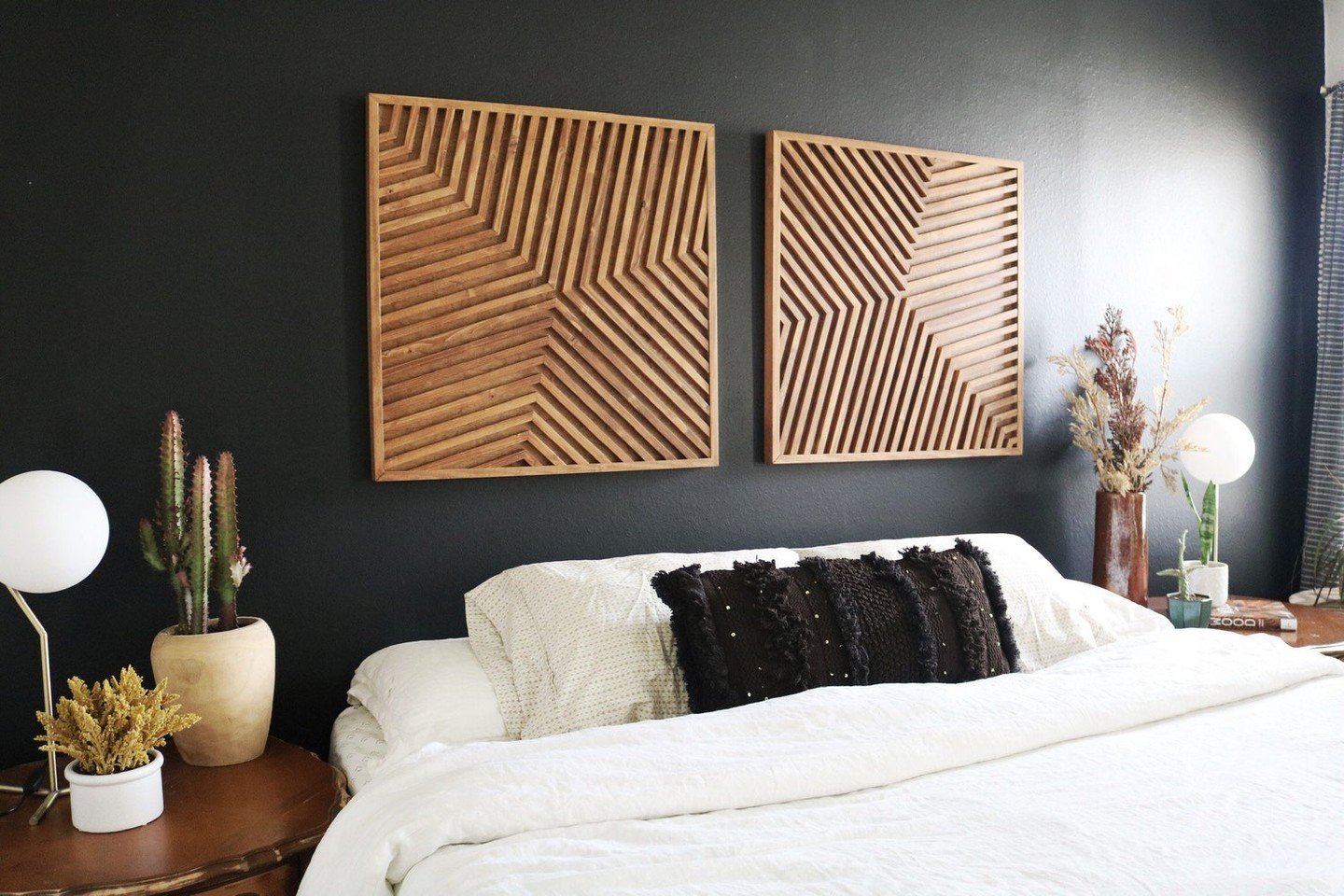 Two square wooden geometric wall art panels hanging above a bed on a black wall
