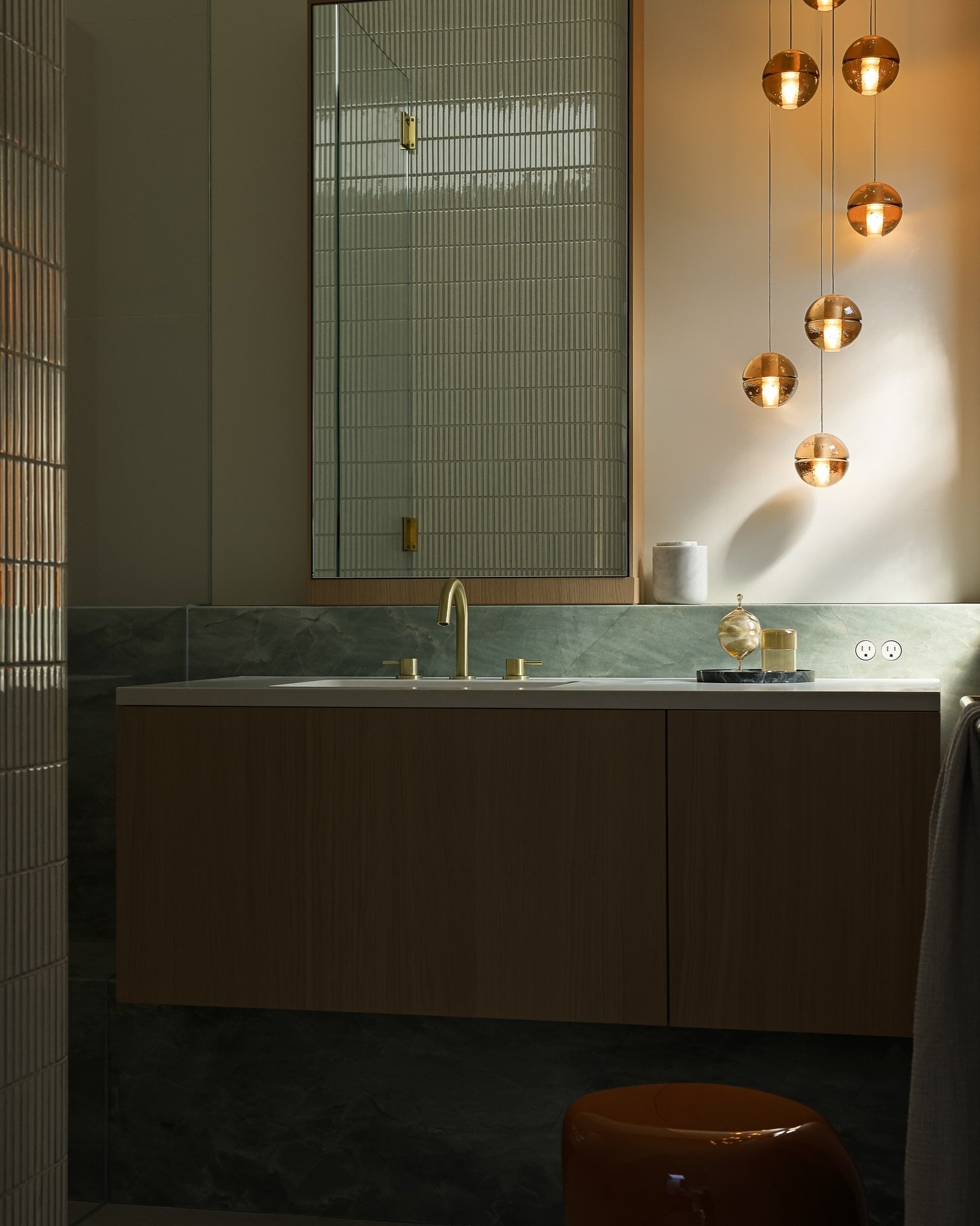 Green marble bathroom accent wall featuring cluster of amber glass pendant lights next to wood mirror