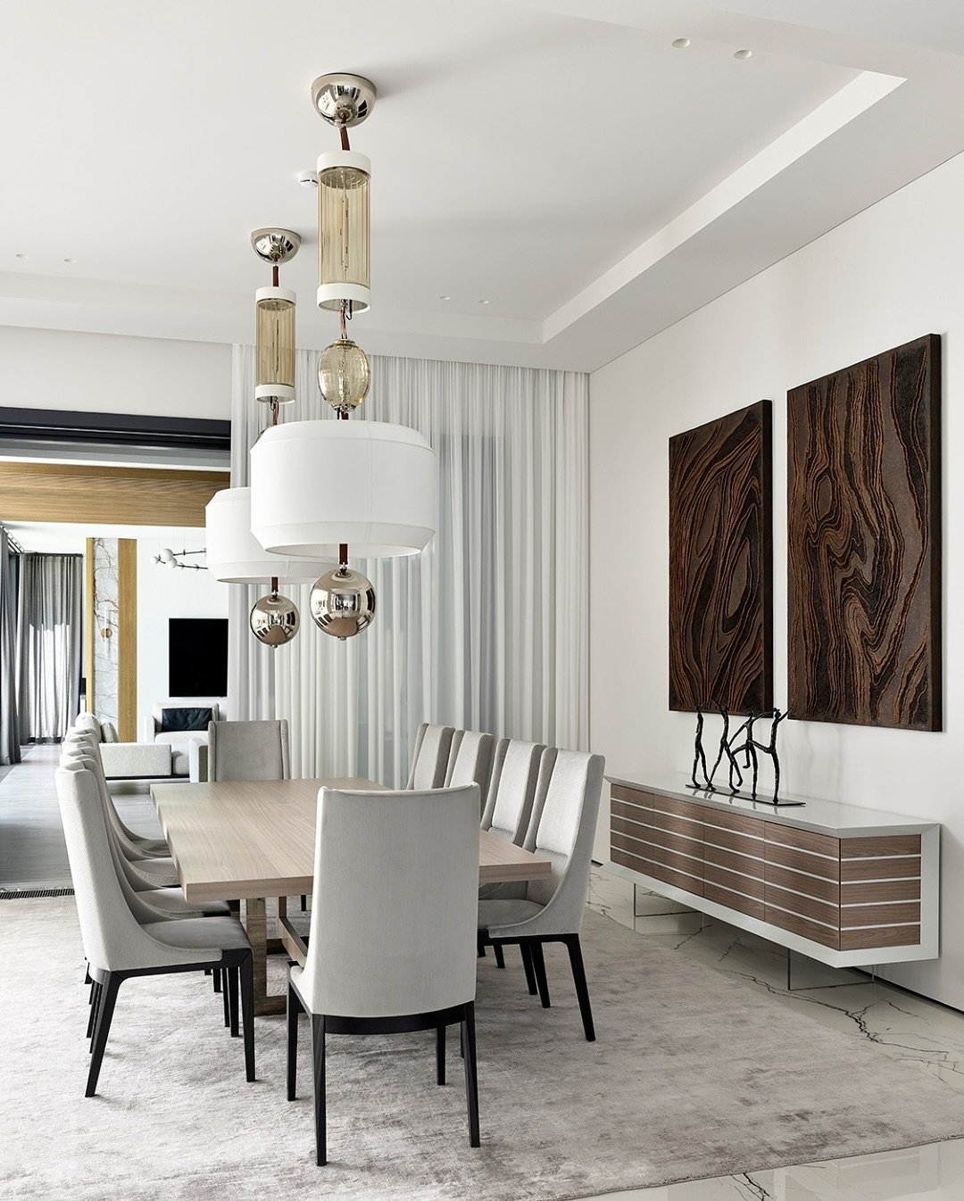 Modern cylinder and drum pendants over light wood dining table with dark wall art.