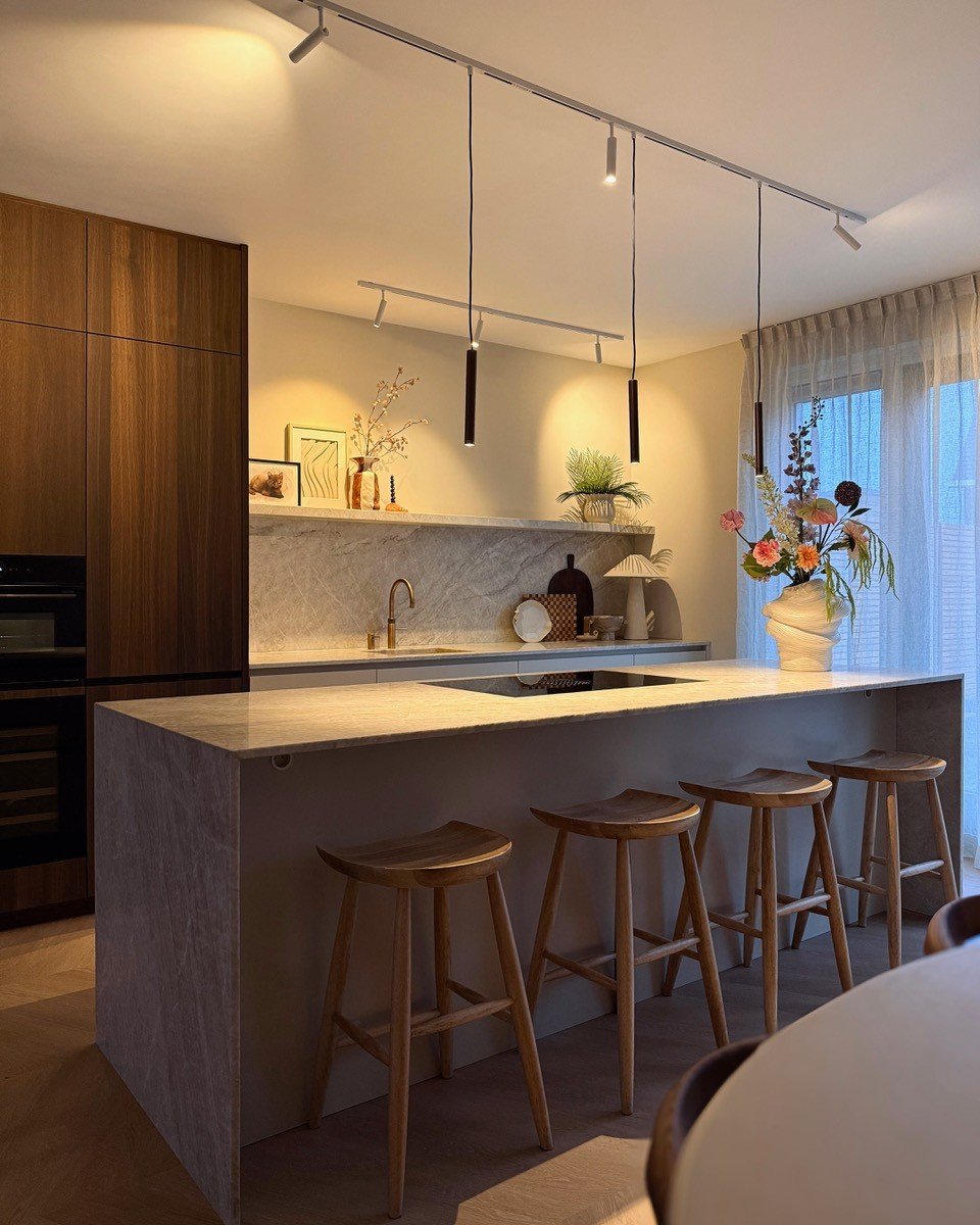 Kitchen island illuminated by three slim black pendant lights with white track lighting washing the back wall.