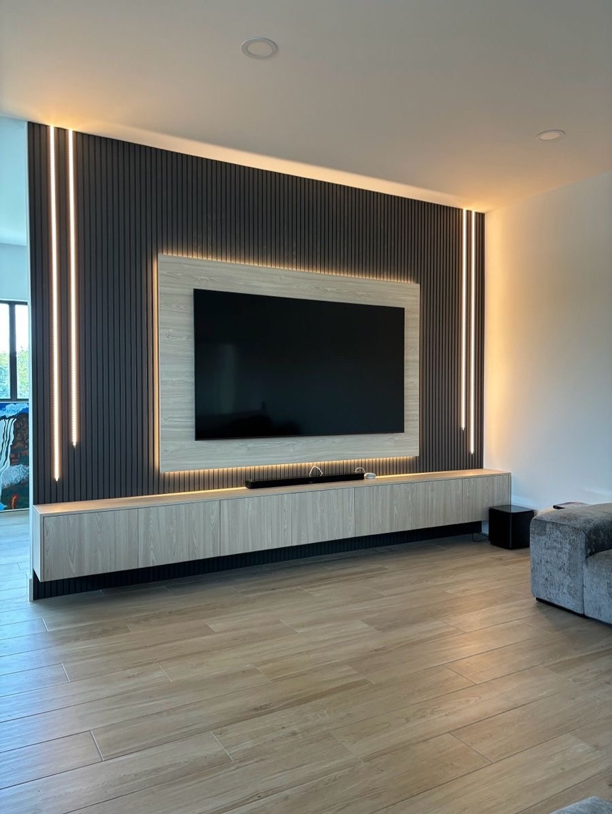 Dark fluted accent wall with light wood floating console and vertical LED strips.