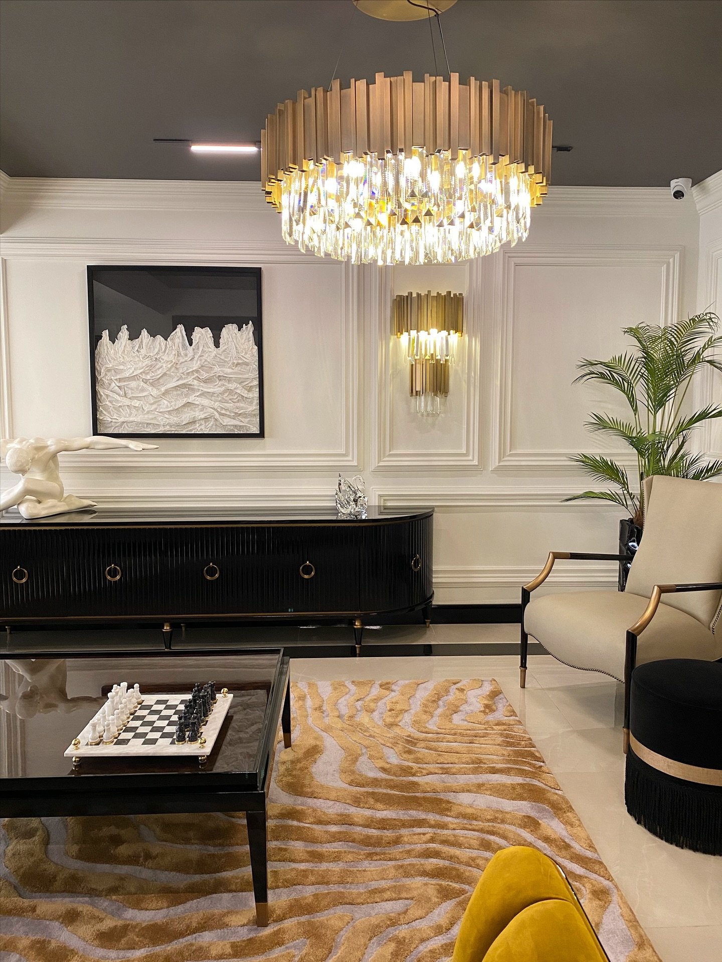 Luxurious living room featuring a gold tiered crystal chandelier hanging from a dark ceiling above a patterned rug.