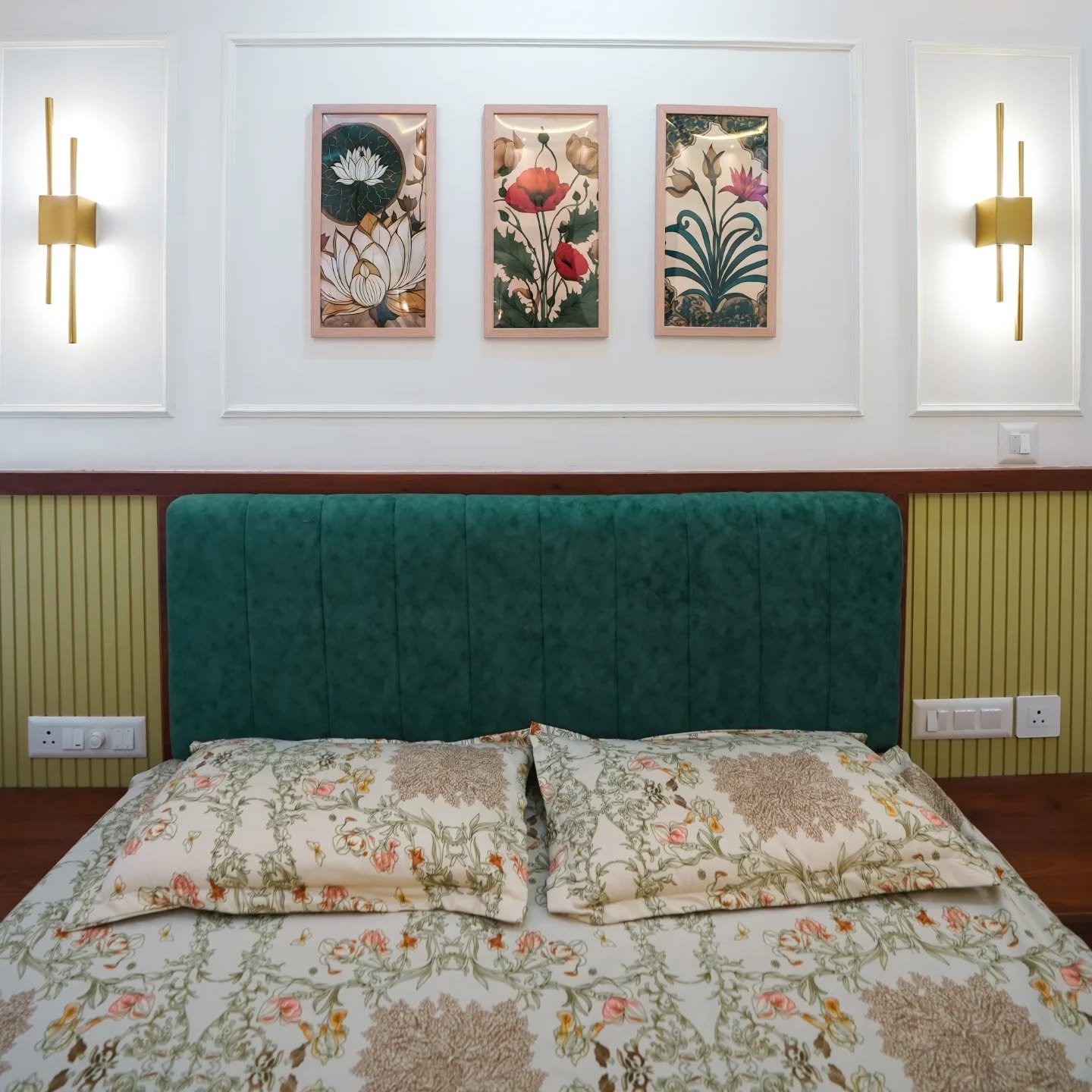 Three floral artworks framed by white wall molding above green velvet headboard