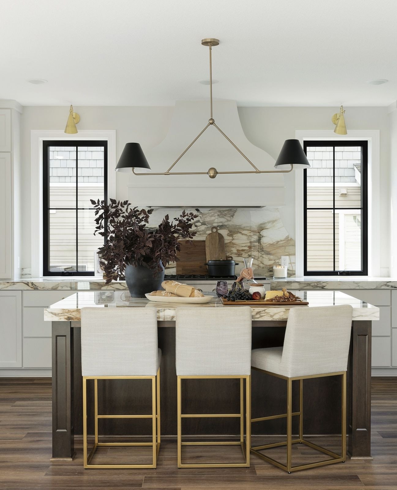 Linear brass light fixture with black cone shades over a marble island.