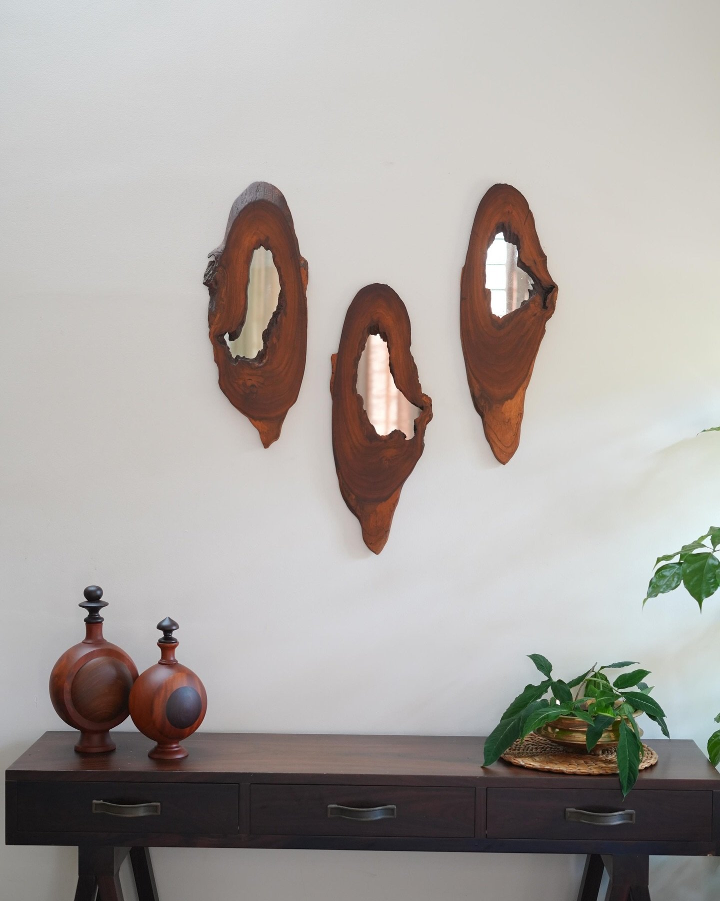 Three irregular wooden wall mirrors hanging above a dark console table with decorative bottles