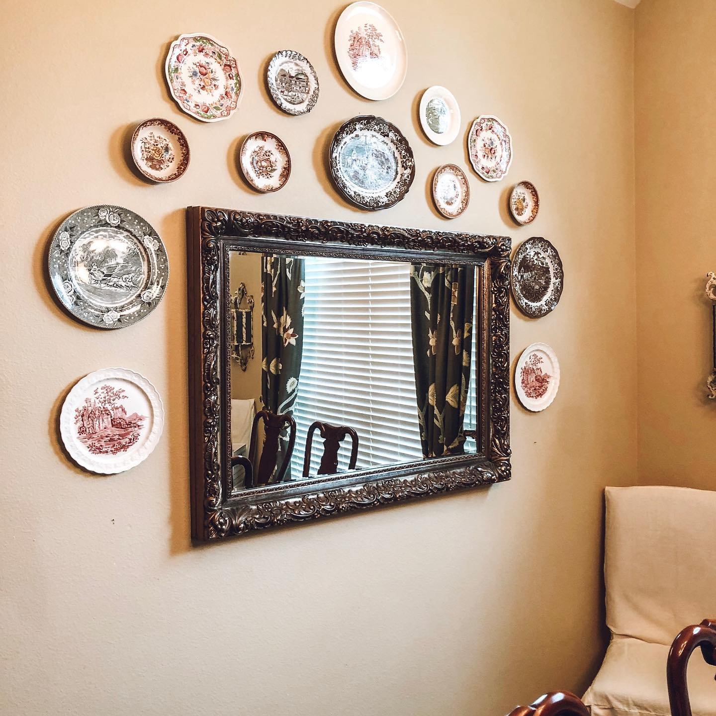 Beige wall featuring a dark ornate mirror crowned by an arch of red, brown and grey transferware plates