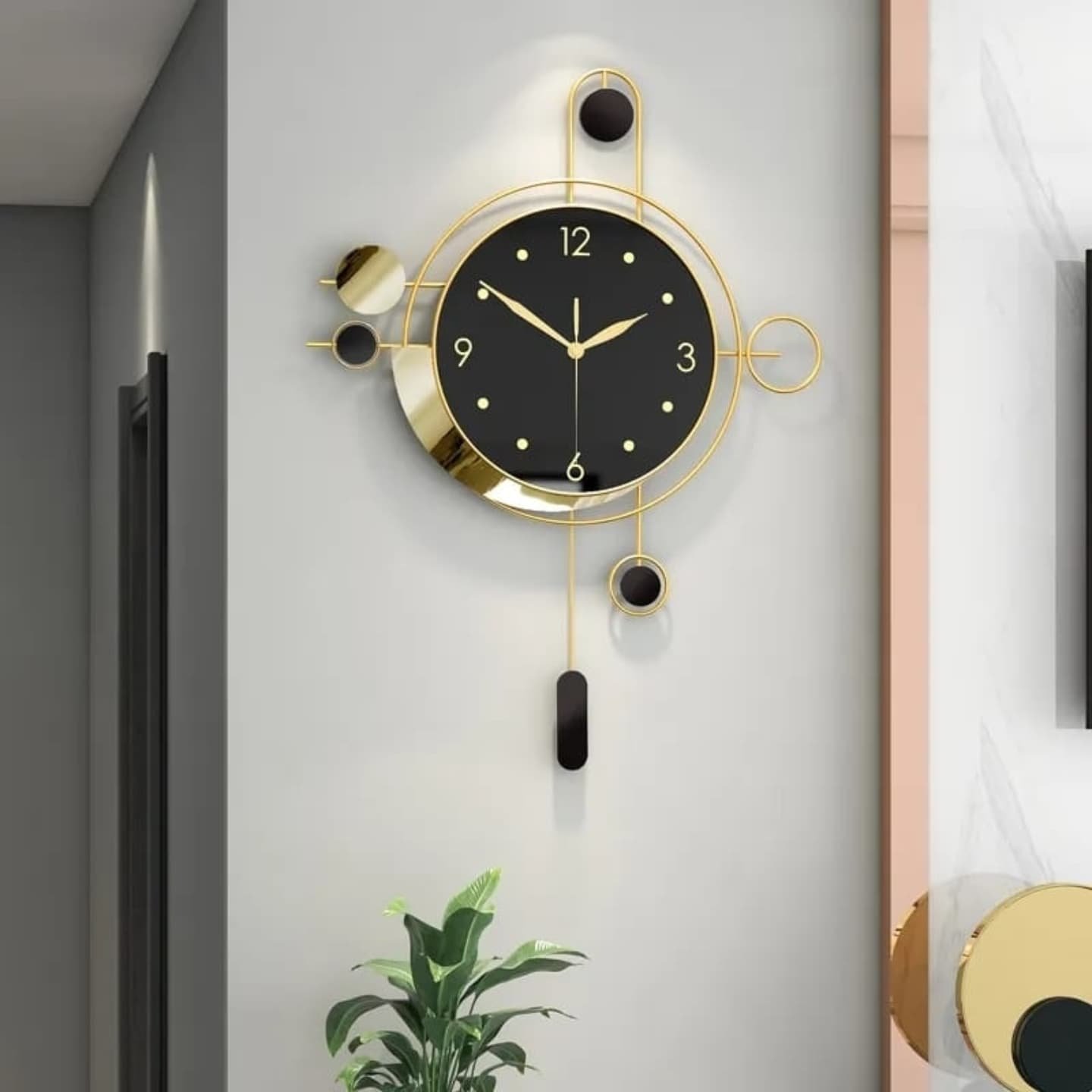 Black and gold wall clock with pendulum mounted on a light grey hallway wall above a plant