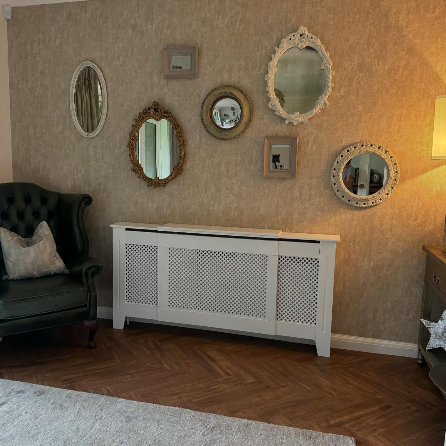 Collection of small vintage mirrors with white and gold frames hanging above a white radiator cover on textured wallpaper.