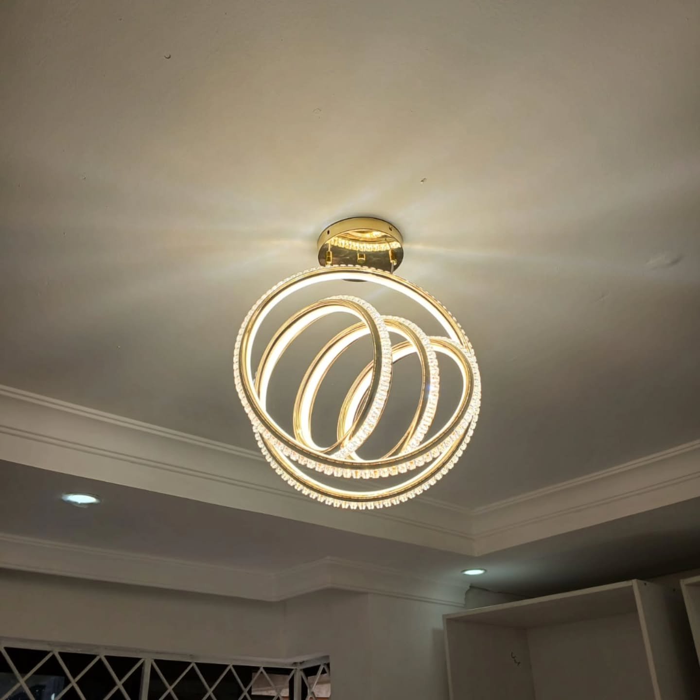 Modern gold LED ceiling light featuring three interlocking crystal rings illuminated against a white ceiling.