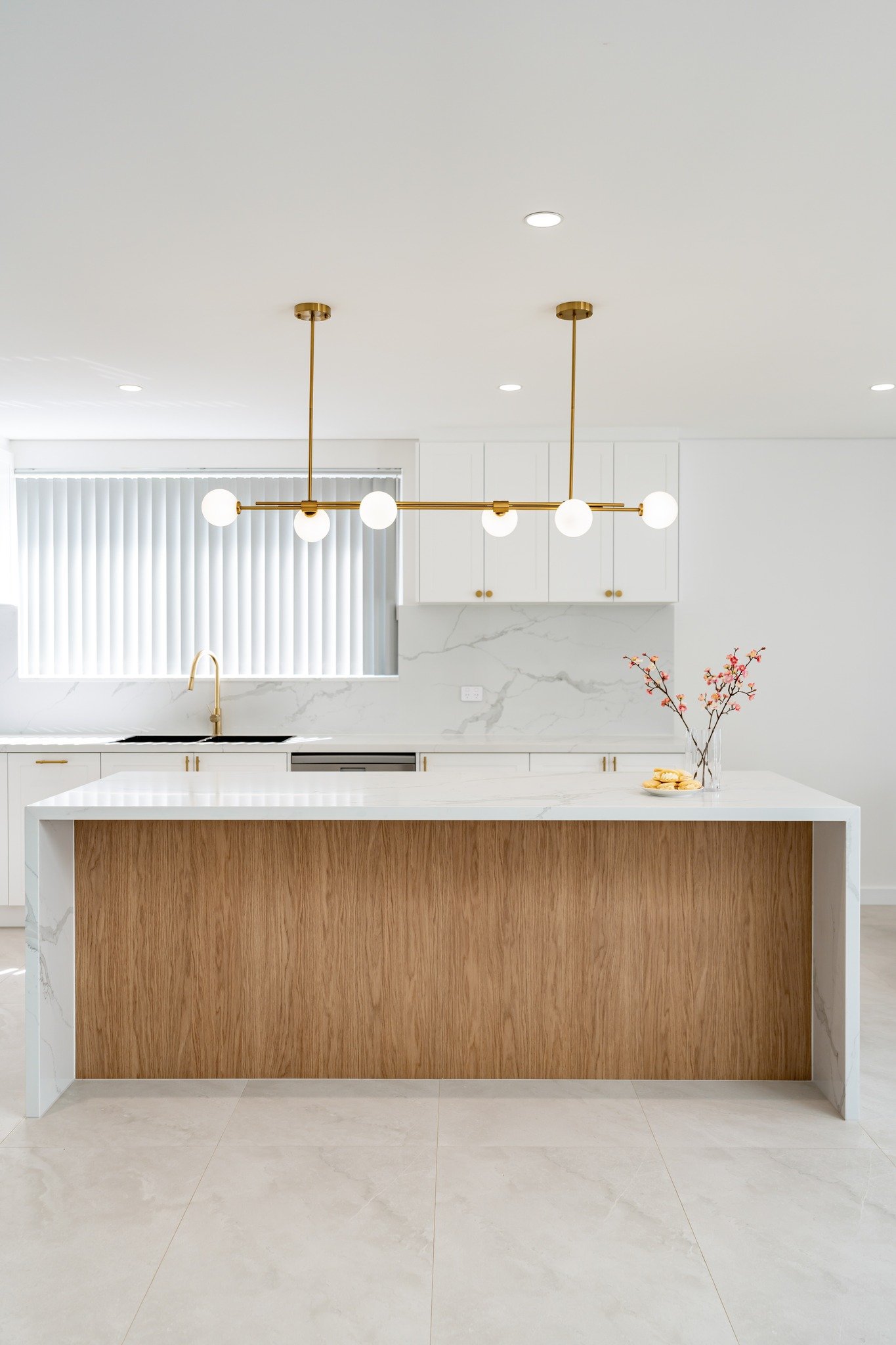 Linear brass fixture with white glass globes hanging over a white and wood waterfall island.