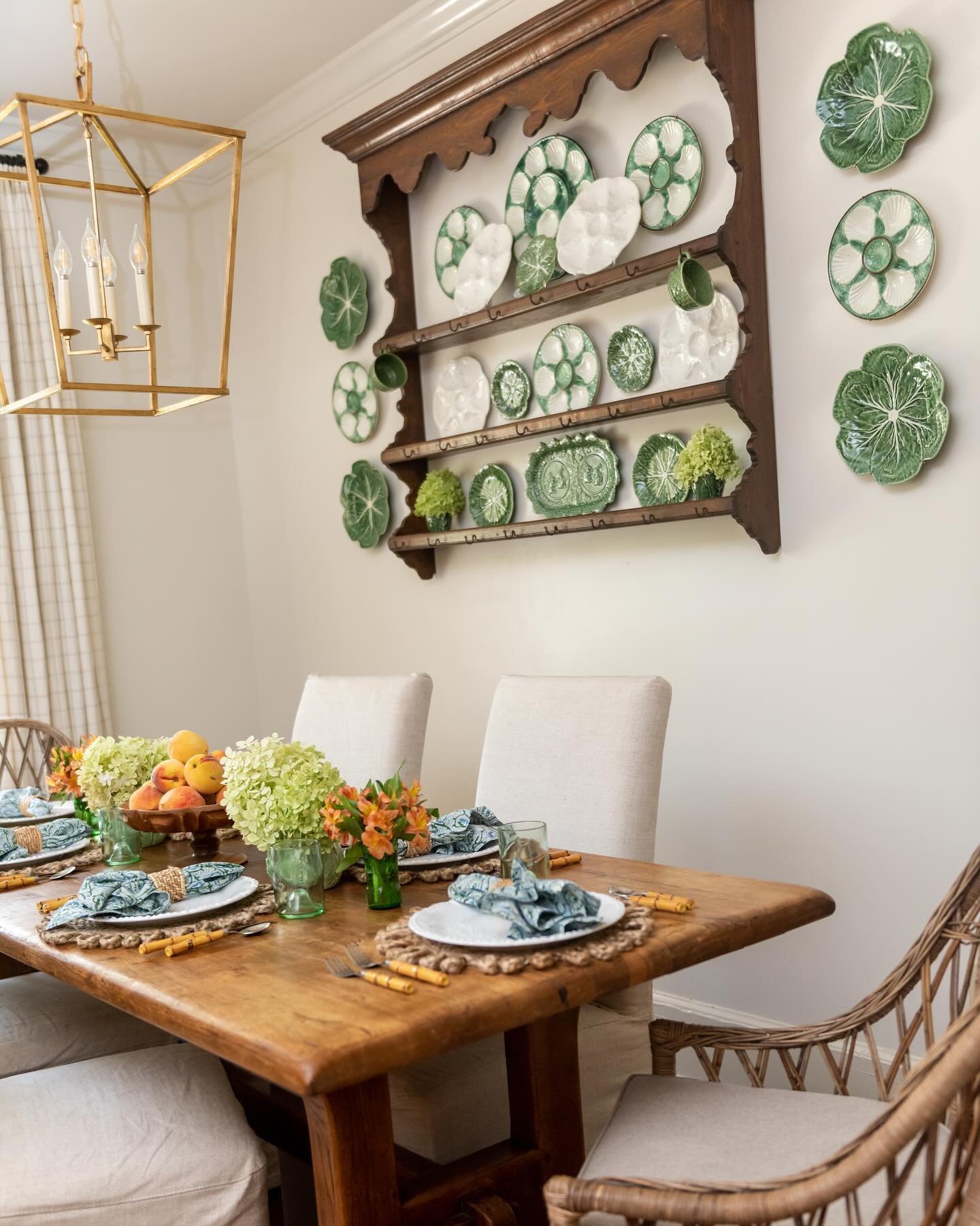 Dining room wall featuring a dark wood plate rack filled with green cabbage and white oyster plates next to a gold lantern