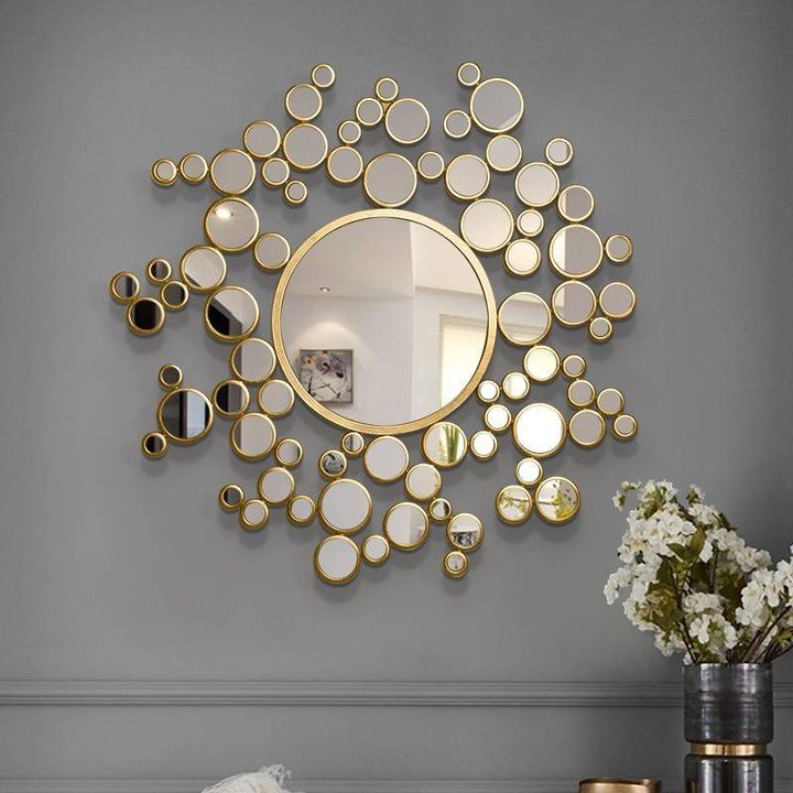 Large central circular mirror surrounded by a cluster of smaller gold-rimmed round mirrors on a grey wall.