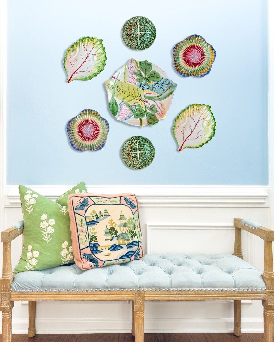 Light blue wall featuring symmetrical arrangement of colorful majolica and leaf plates above a tufted bench